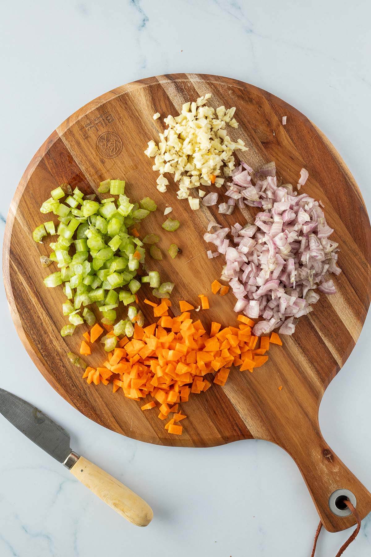 Holzbrett mit fein gew&uuml;rfelten Sellerie, Karotte, Knoblauch und Schalotten.
