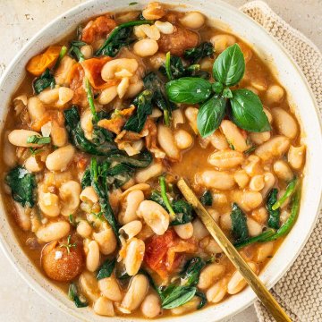 Teller mit einer mediterranen wei&szlig;en Bohnenpfanne in Tomatensauce mit Spinat, serviert mit Brot und frischem Basilikum.
