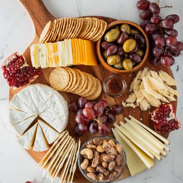 K&auml;seplatte mit verschiedenen K&auml;sesorten, Crackern, Trauben, Oliven, N&uuml;ssen und Granatapfel von oben fotografiert.