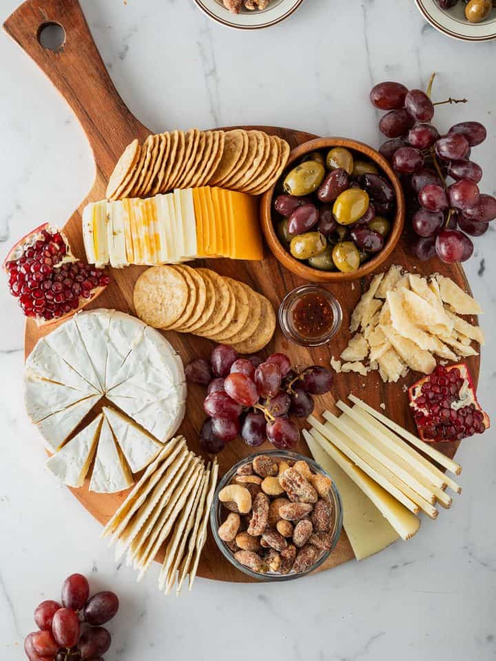 K&auml;seplatte mit verschiedenen K&auml;sesorten, Crackern, Trauben, Oliven, N&uuml;ssen und Granatapfel von oben fotografiert.