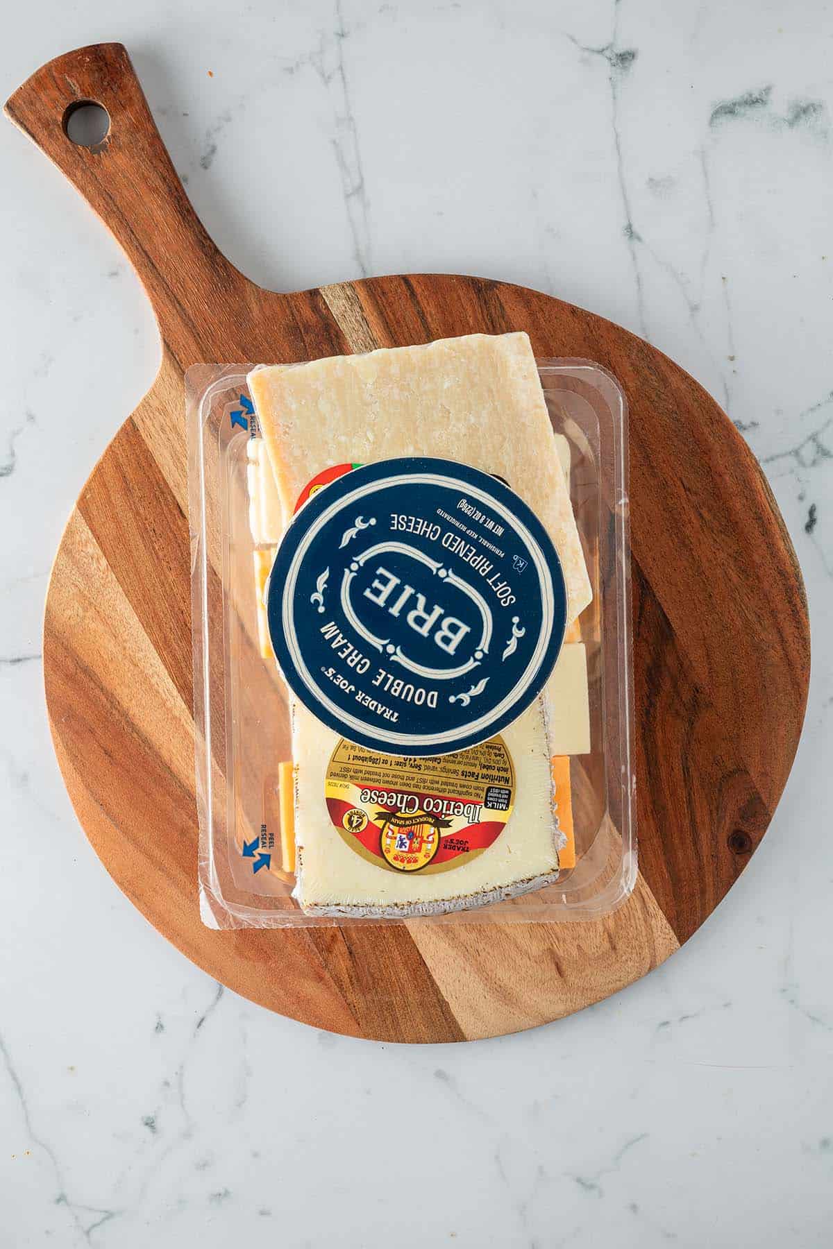 Verpackte K&auml;sesorten auf einem Holzbrett als Ausgangspunkt f&uuml;r eine K&auml;seplatte.