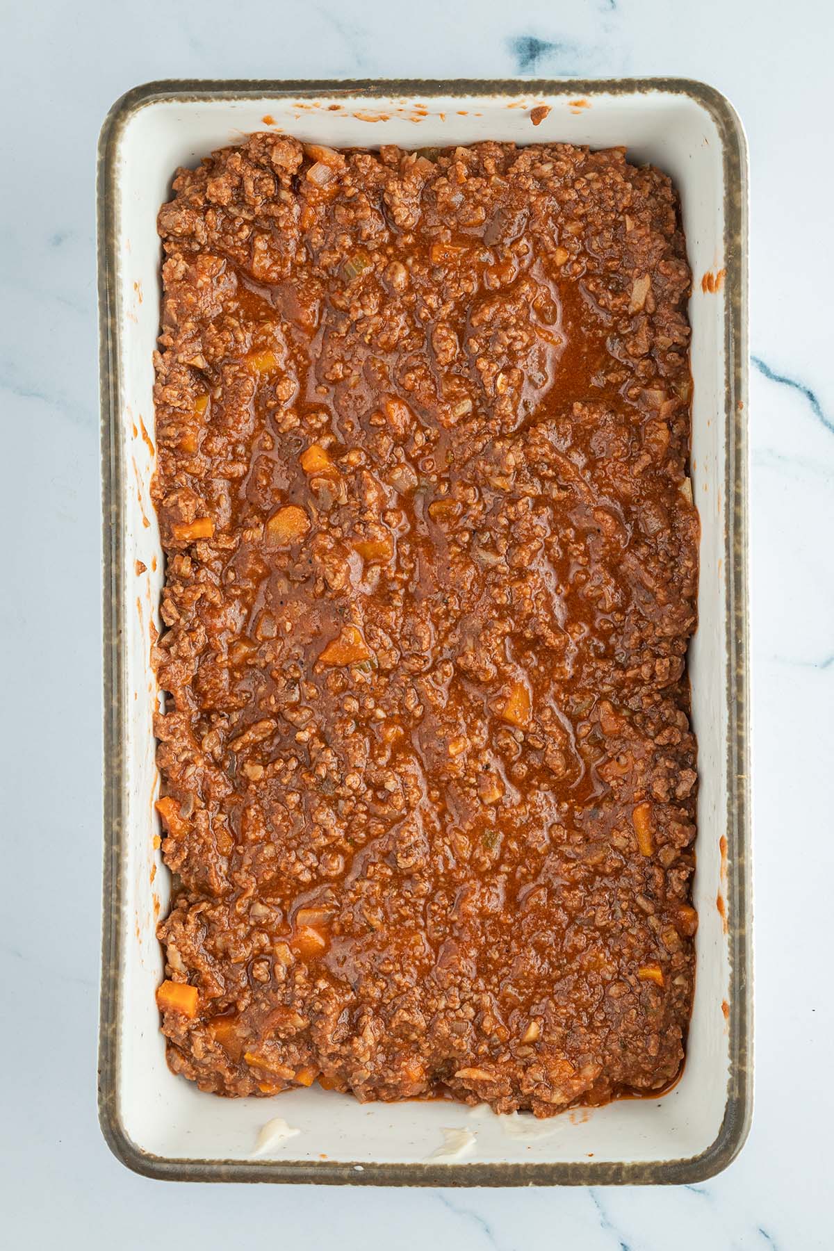 Vogelperspektive auf eine rechteckige Auflaufform, wo eine Schicht Bolognese die restlichen Schichten bedeckt.