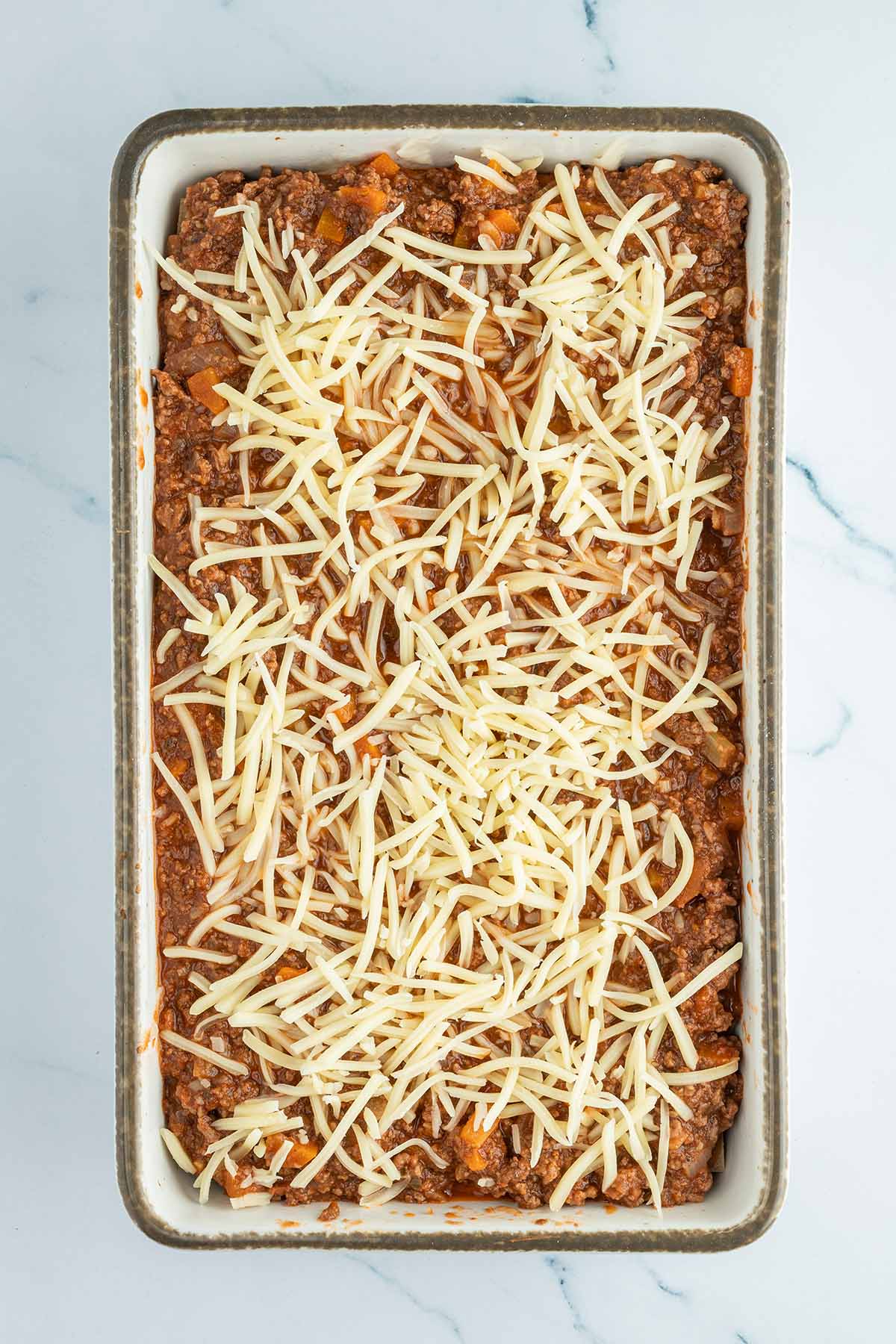 Auflaufform mit einer Lasagne vor dem Backen und reichlich geraspelter Mozzarella auf der Oberfl&auml;che.
