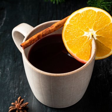Eine Tasse Gl&uuml;hwein mit einer Orange und Zimtstange als Deko auf einem dunklen Holzhintergrund.