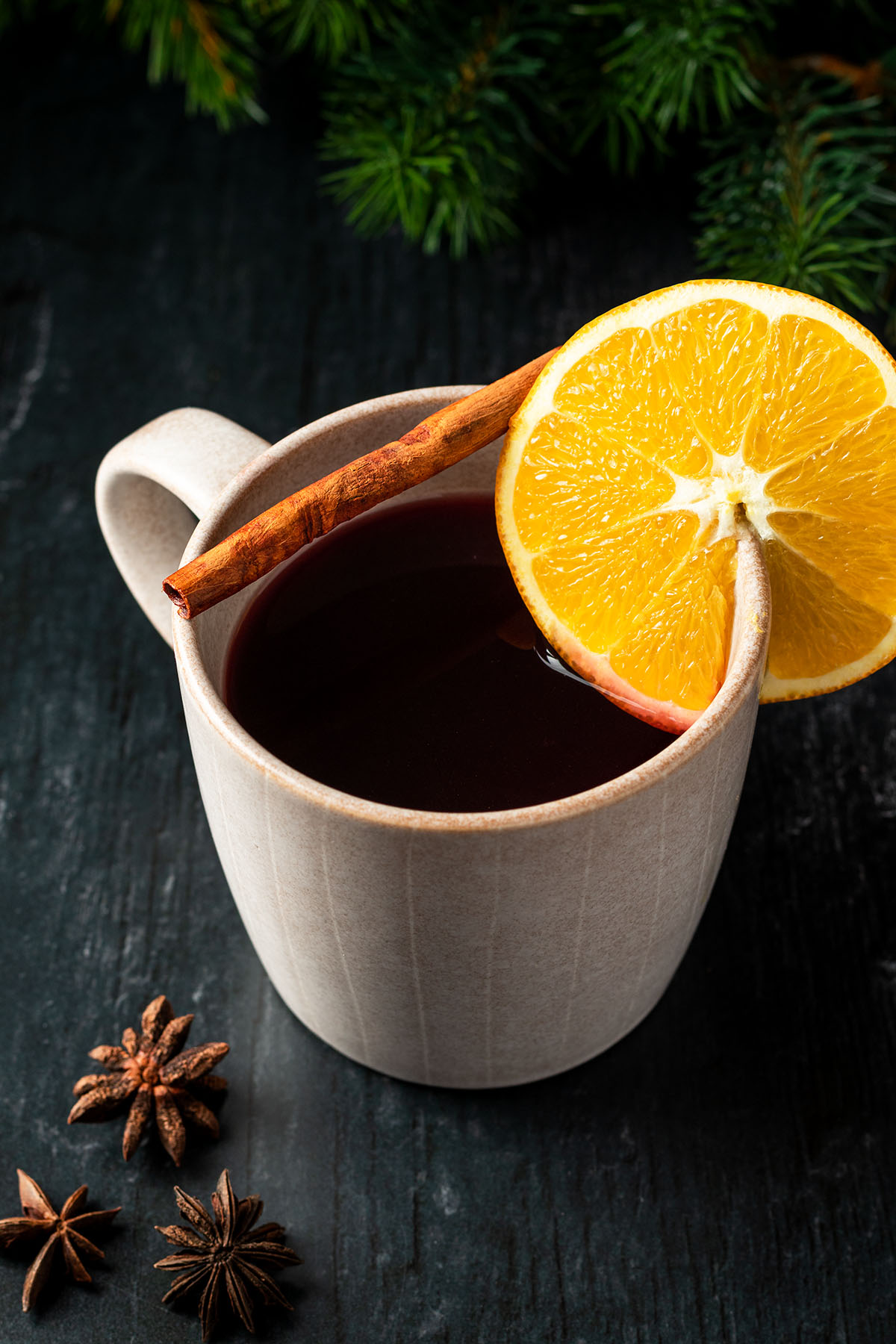 Eine Tasse Gl&uuml;hwein mit einer Orange und Zimtstange als Deko auf einem dunklen Holzhintergrund.