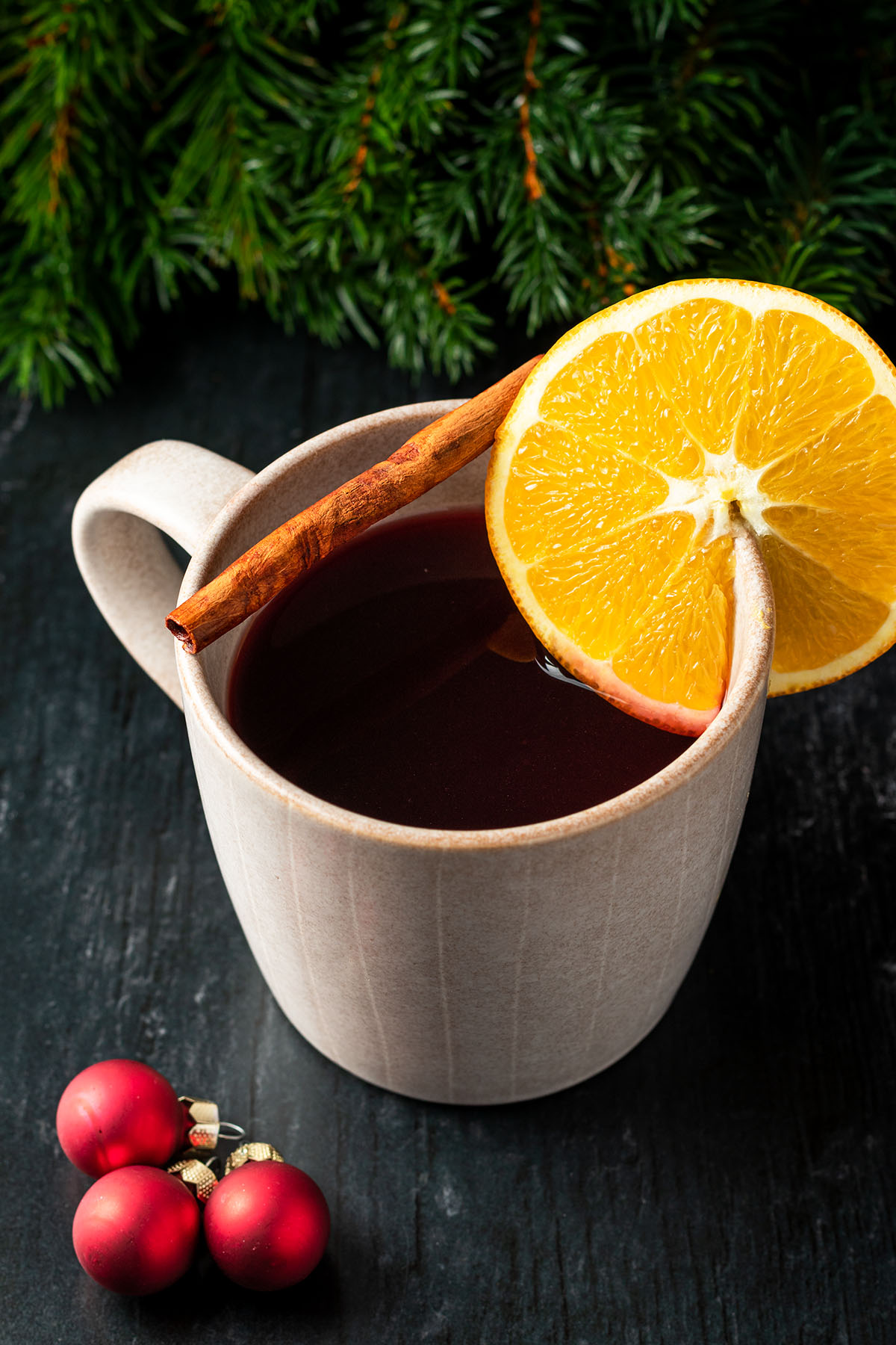 Eine Tasse mit Gl&uuml;hwein, einer Orange und Zimtstange umgeben von weihnachtlicher Deko.