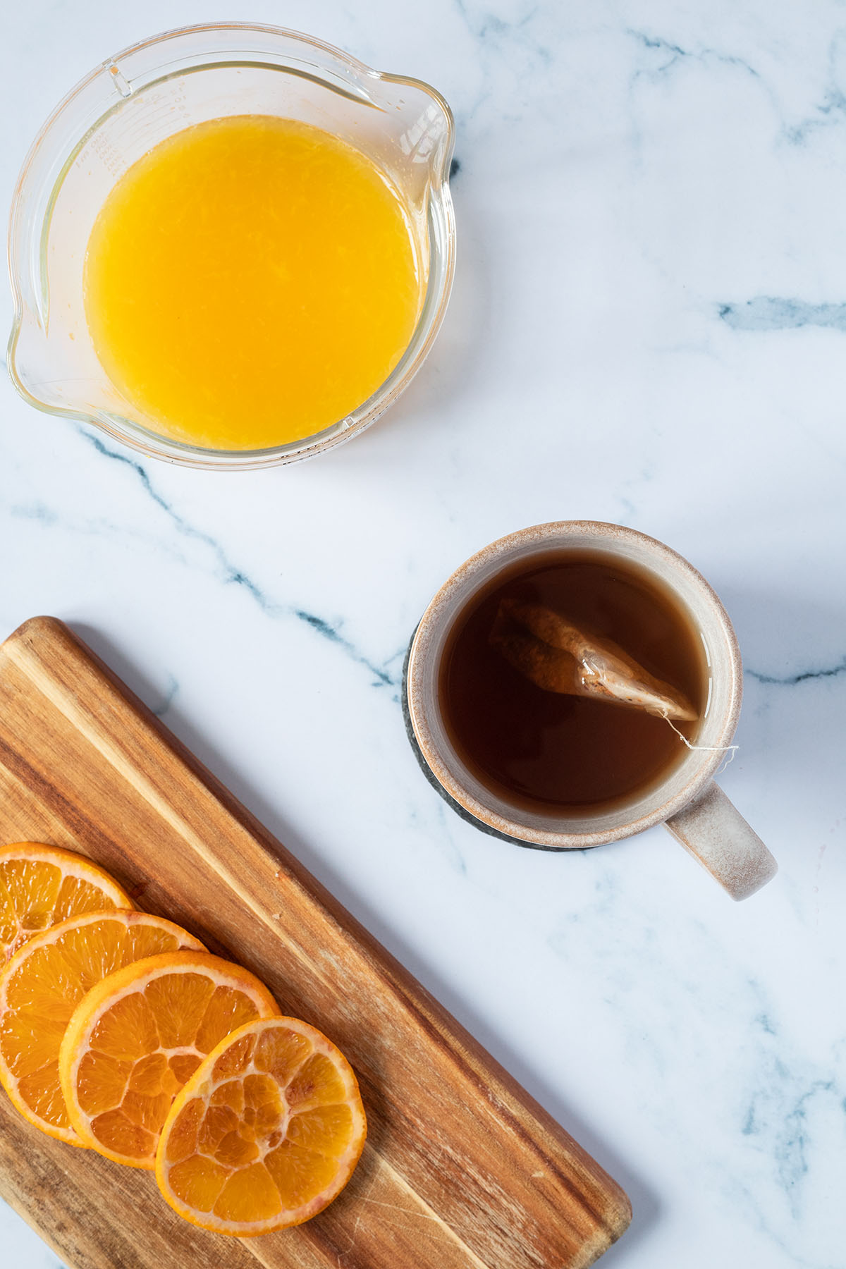 Vogelperspektive auf eine Tasse Tee, ein Brett mit in Scheiben geschnittenen Orangen und ein Messbecher mit frischgepressten Orangensaft.