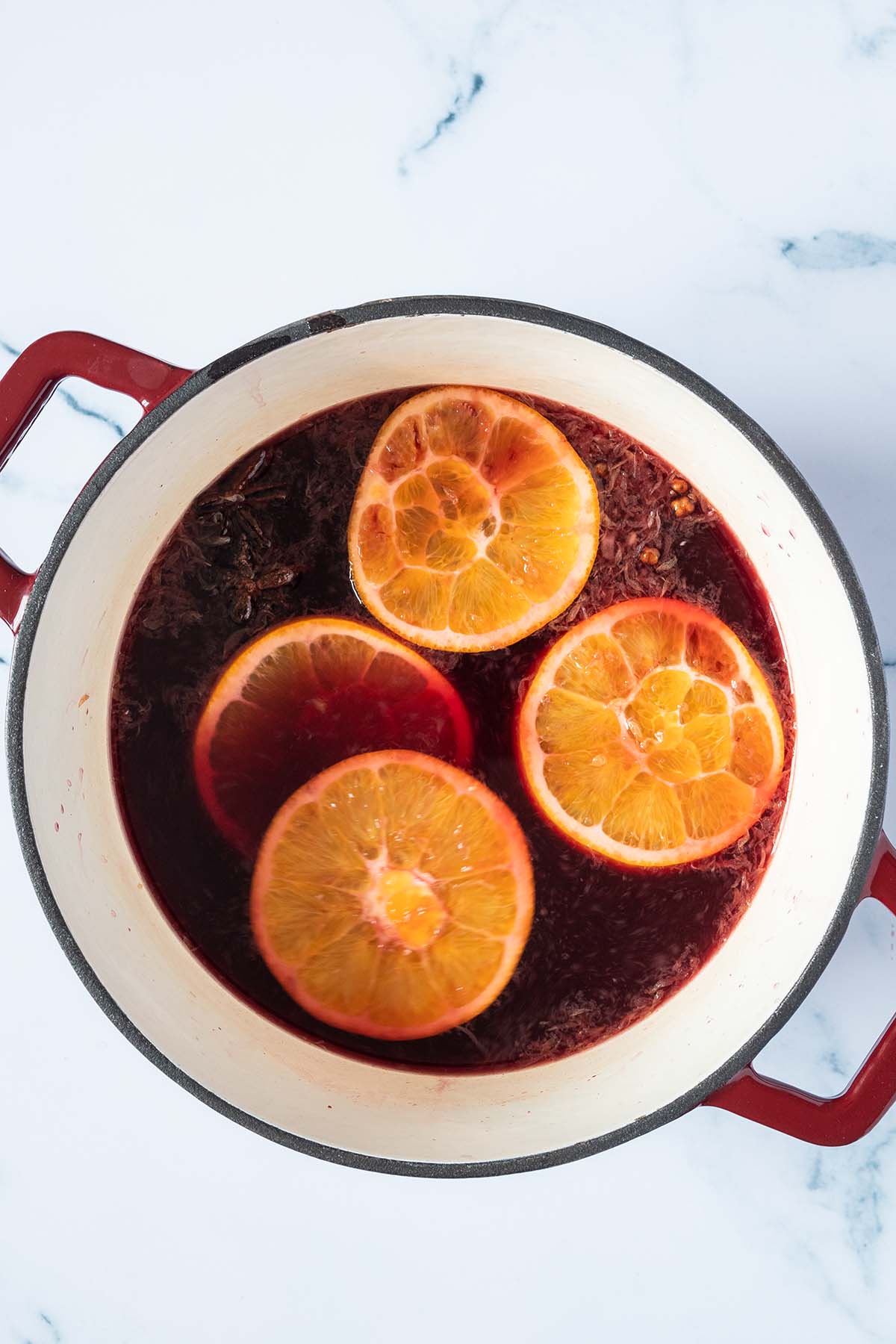 Vogelperspektive auf einen Topf mit Rotwein, Gew&uuml;rze und Orangen.