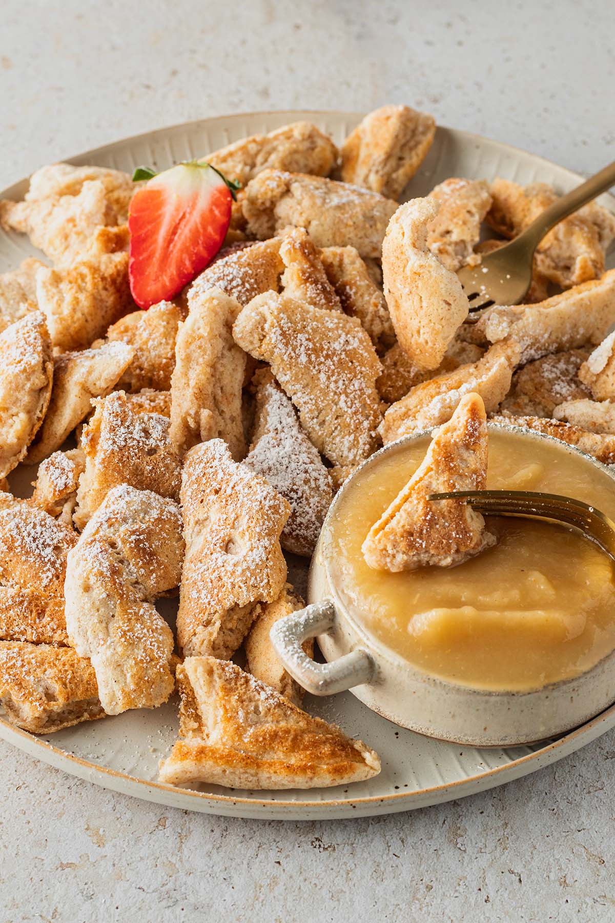 Ein Teller mit Kaiserschmarren, einer Sch&uuml;ssel Apfelmus und einer Erdbeere.