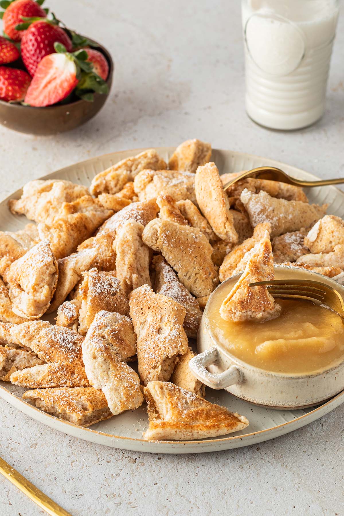 Kaiserschmarrn serviert auf einem gro&szlig;en Teller mit zwei Gabeln und Apfelmus, Deko im Hintergrund des Bildes.