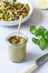 Kalorienarmes und gesundes Pesto mit Basilikum in einem kleinen Weck-Gl&auml;schen, im Hintergrund ein Teller Nudeln.