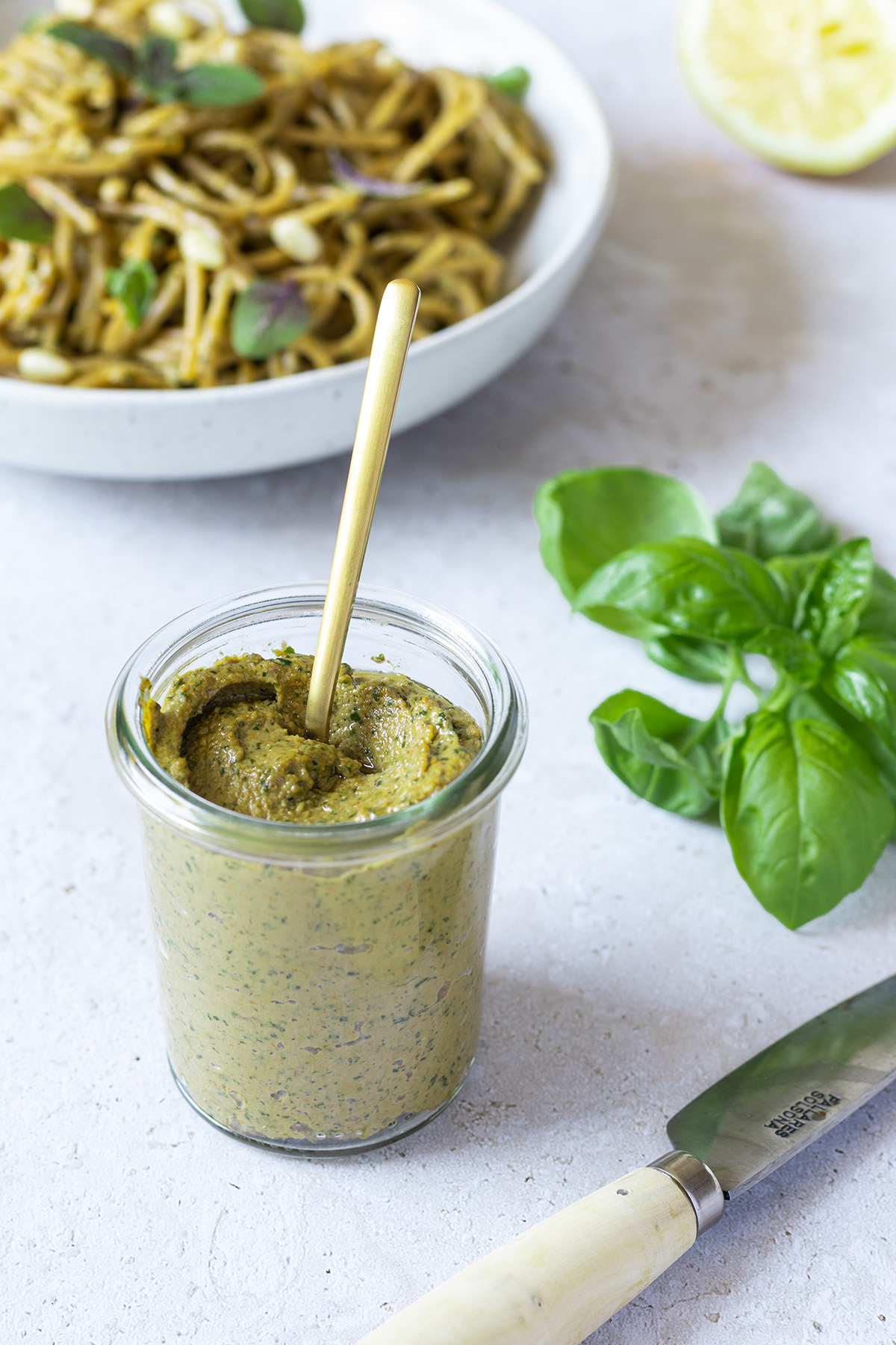 Kalorienarmes und gesundes Pesto mit Basilikum in einem kleinen Weck-Gl&auml;schen, im Hintergrund ein Teller Nudeln.