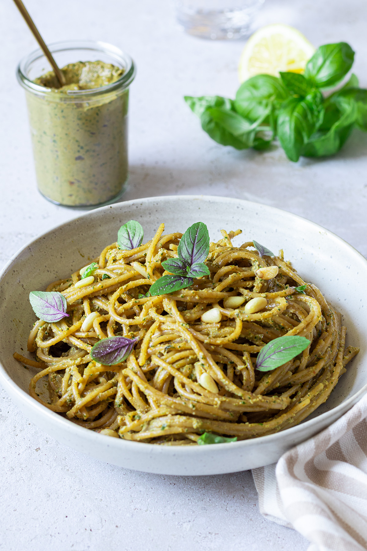 Ein Teller mit Spaghetti mit selbstgemachte, kalorienarmer Pesto. Im Hintergrund ein Gl&auml;schen Pesto und frischer Basilikum.