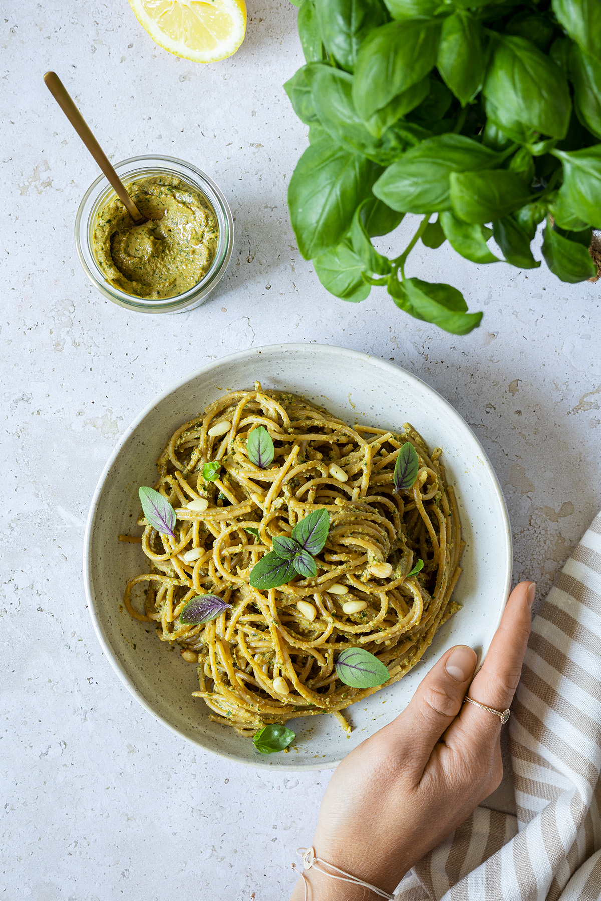 Ein Teller Spaghetti mit gesunder, kalorienarmer Pesto, daneben ein Topf Basilikum und ein Glas mit dem selbstgemachten, gesunden Pesto.