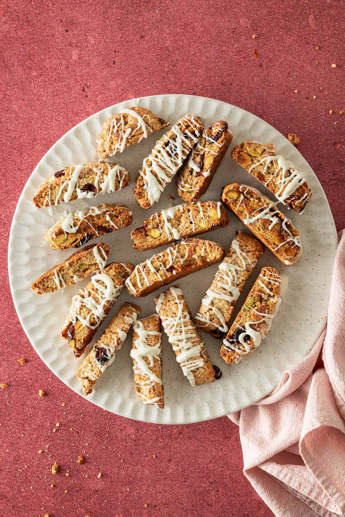 Kardamom-Cantuccini mit Cranberries und Pistazien auf einem Teller, mit wei&szlig;er Schokolade dekoriert.