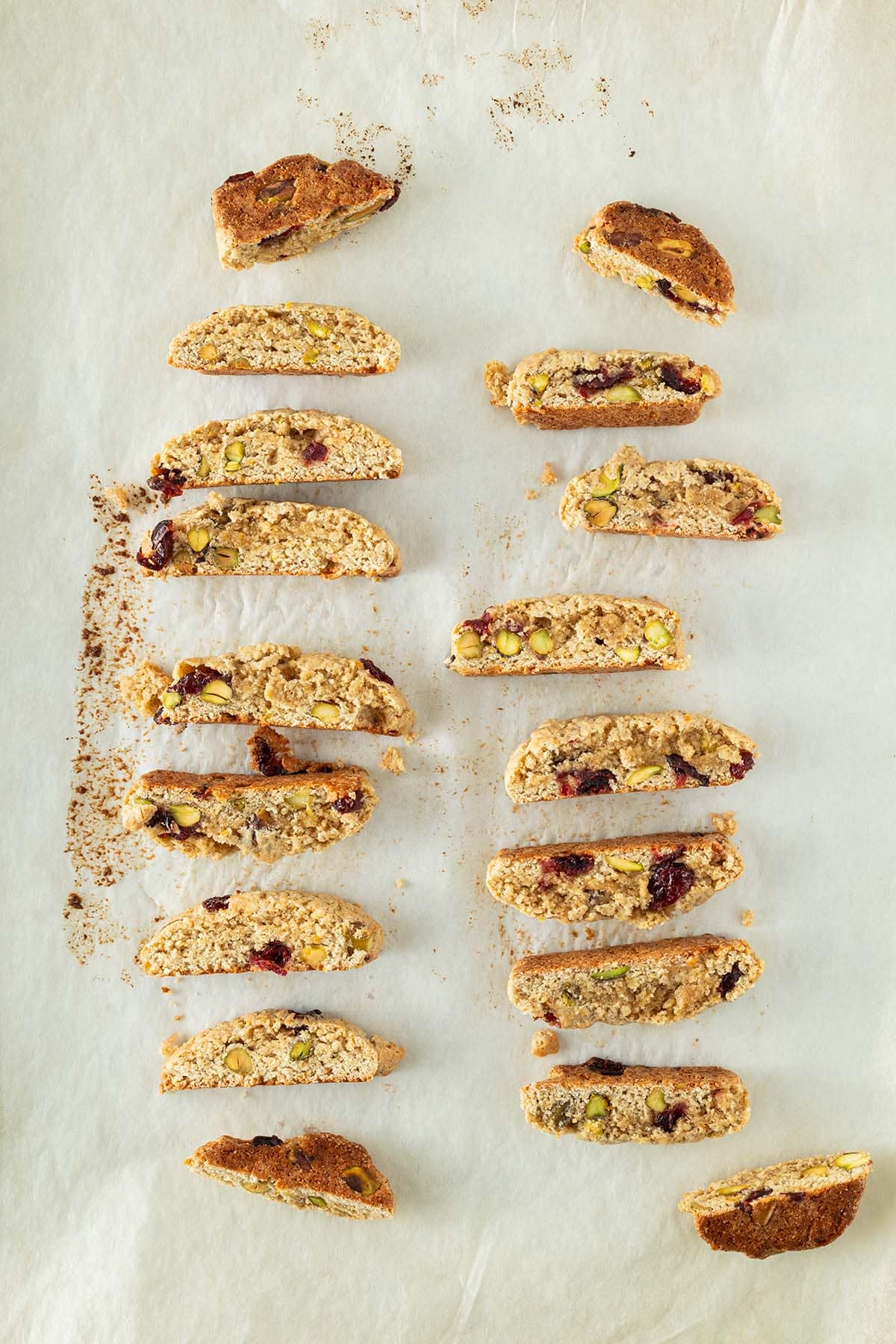 Aufgeschnittene Kardamom-Pl&auml;tzchen mit Cranberries und Pistazien, gleichm&auml;&szlig;ig auf Backpapier verteilt.