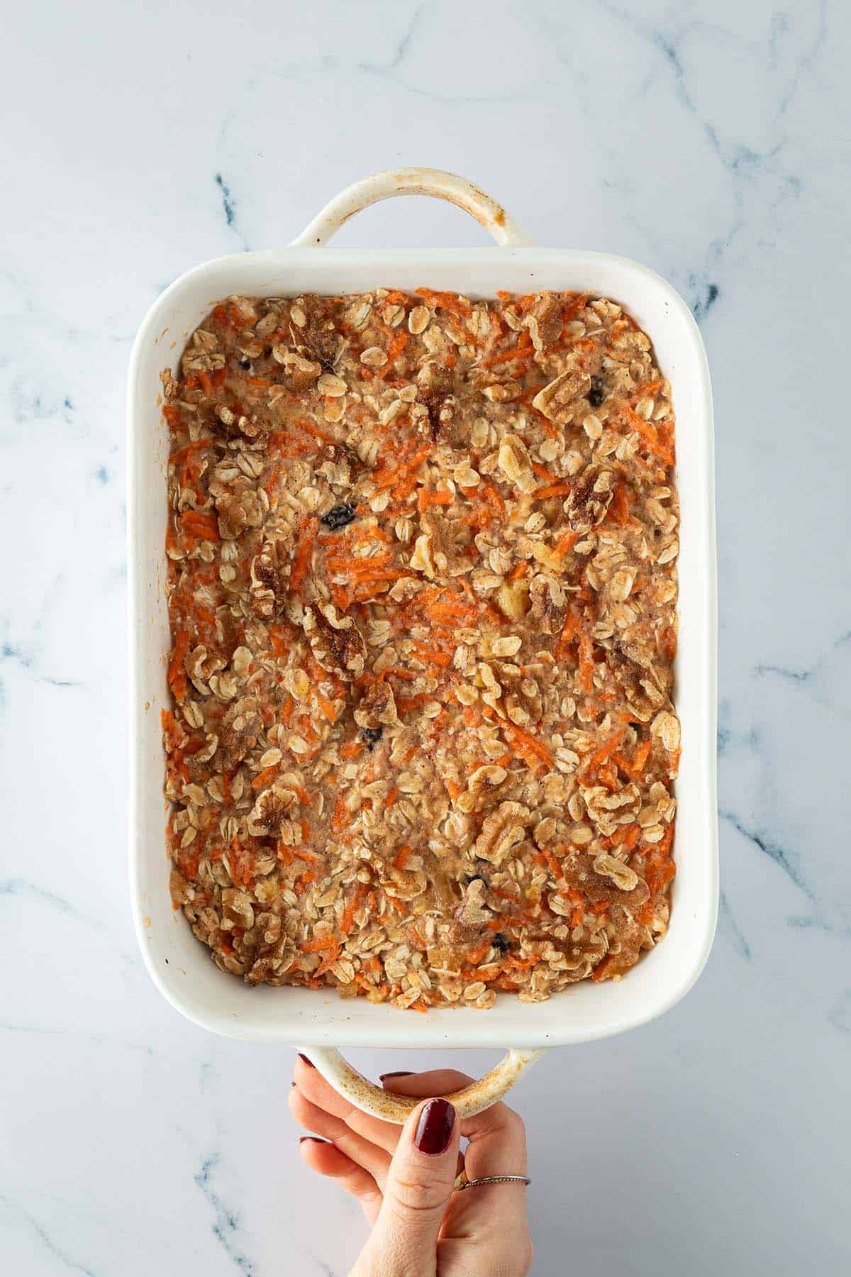 Ungebackene Karotten-Baked-Oats-Masse in Auflaufform mit Waln&uuml;ssen auf der Oberfl&auml;che.