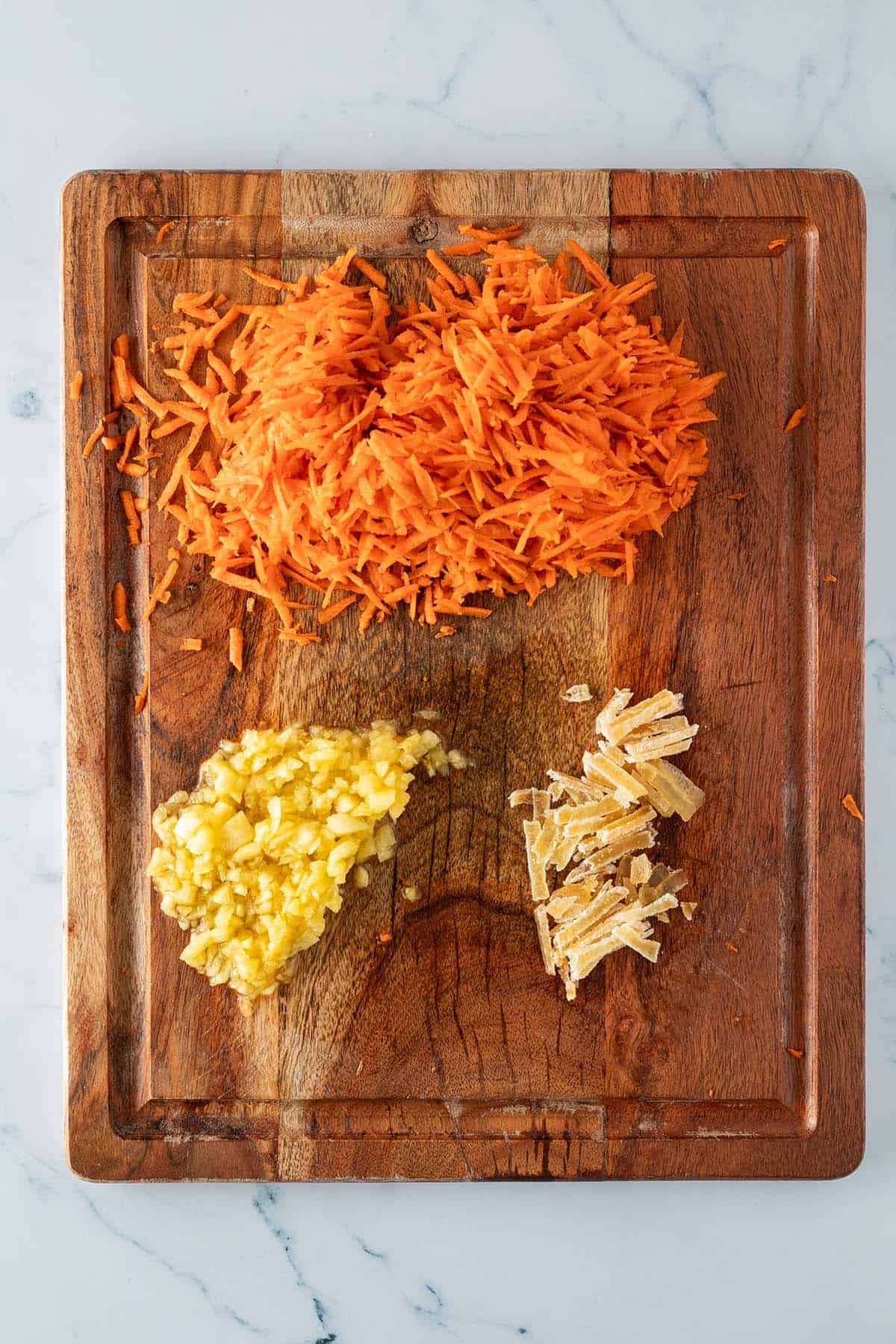 Geraspelte Karotten, fein gehackte Ananas und in d&uuml;nne Streifen geschnittener, kandierter Ingwer auf einem Holzbrett.