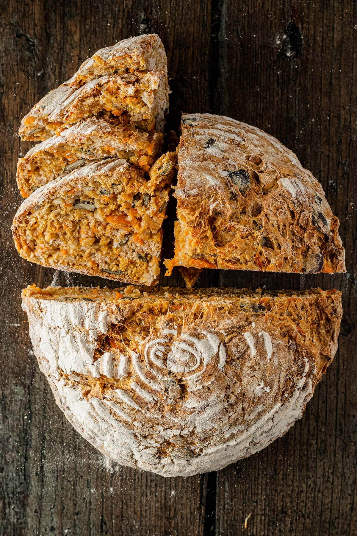 Vogelperspektive auf ein saftiges, teils aufgeschnittenes Karottenbrot, das auf einem rustikalen Holzuntergrund liegt.