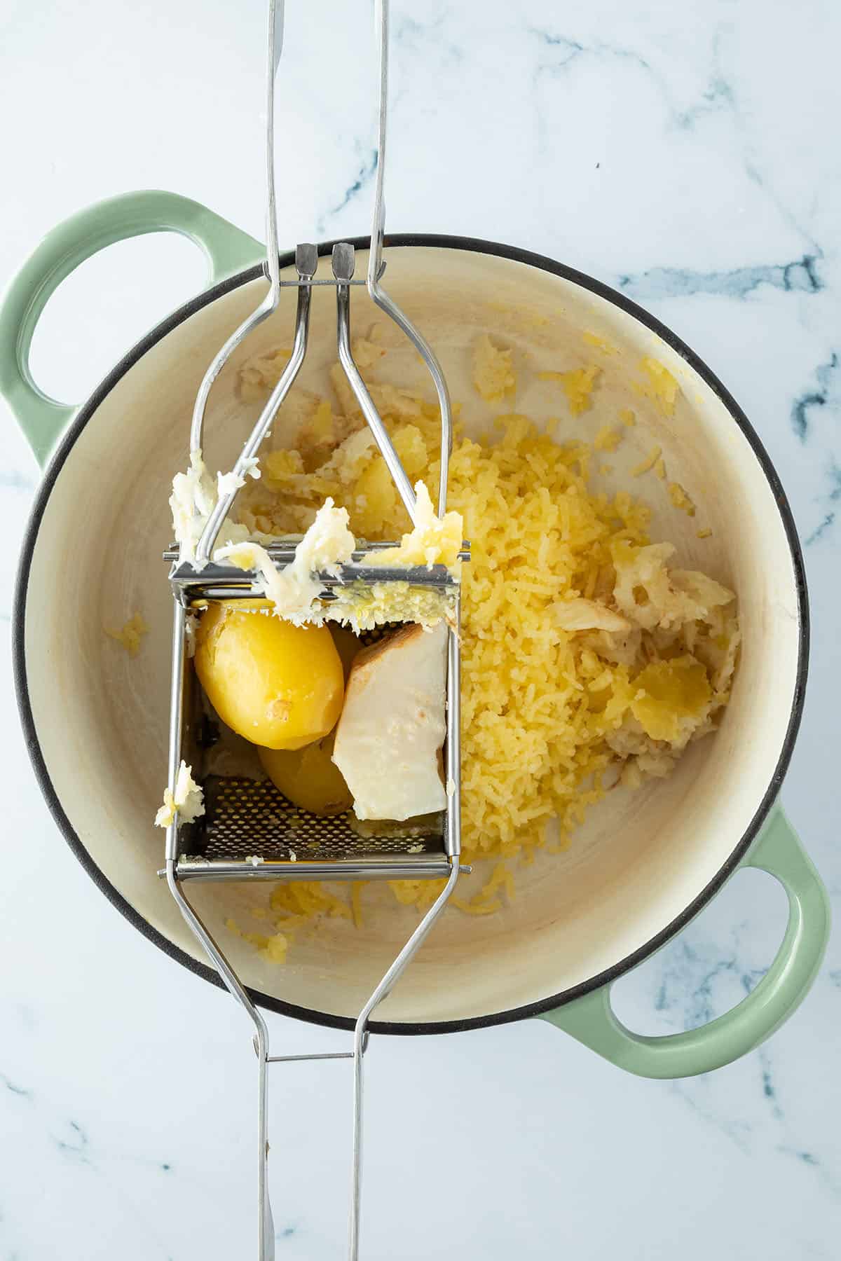 Gekochte Kartoffeln und Selleriest&uuml;cke werden durch eine Kartoffelpresse gedr&uuml;ckt.