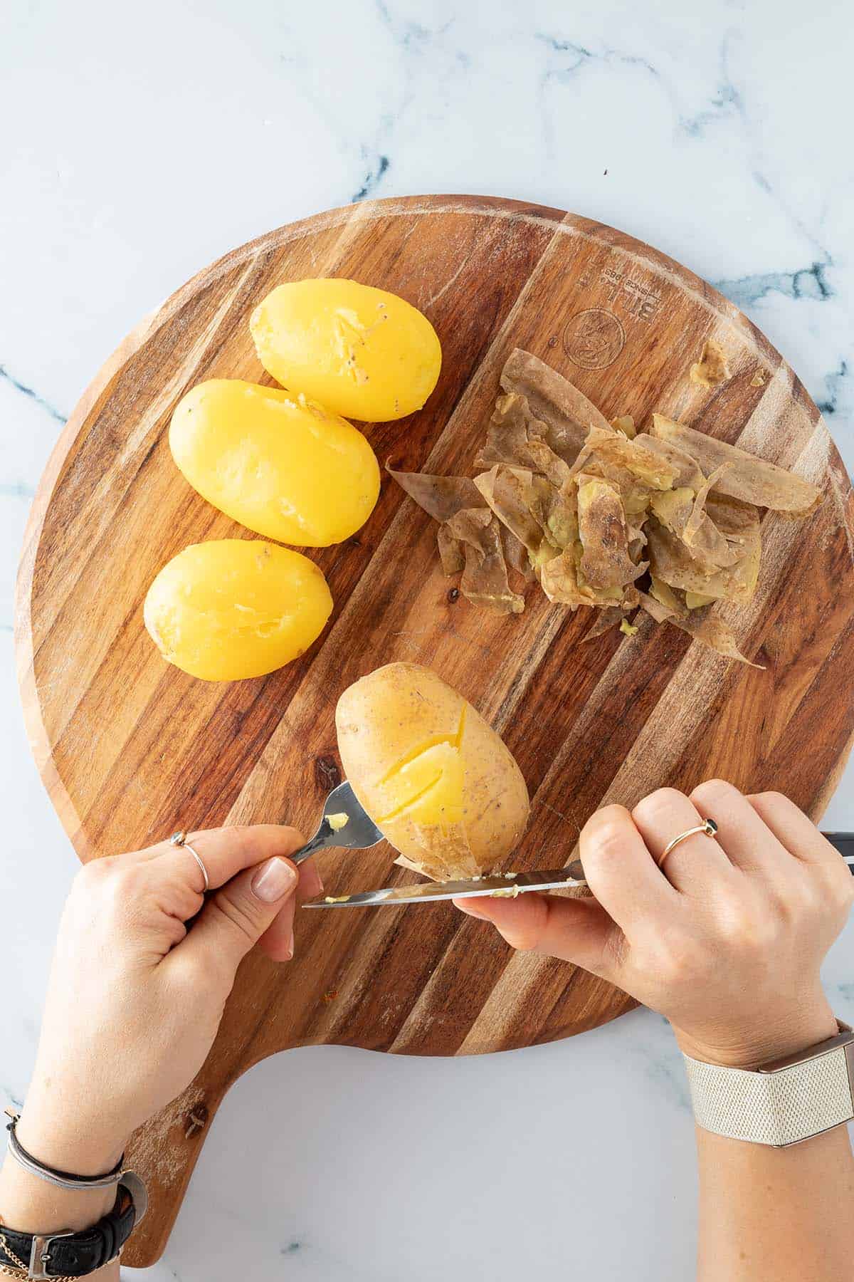 Gekochte Kartoffeln werden mit einem kleinen K&uuml;chenmesser gesch&auml;lt.