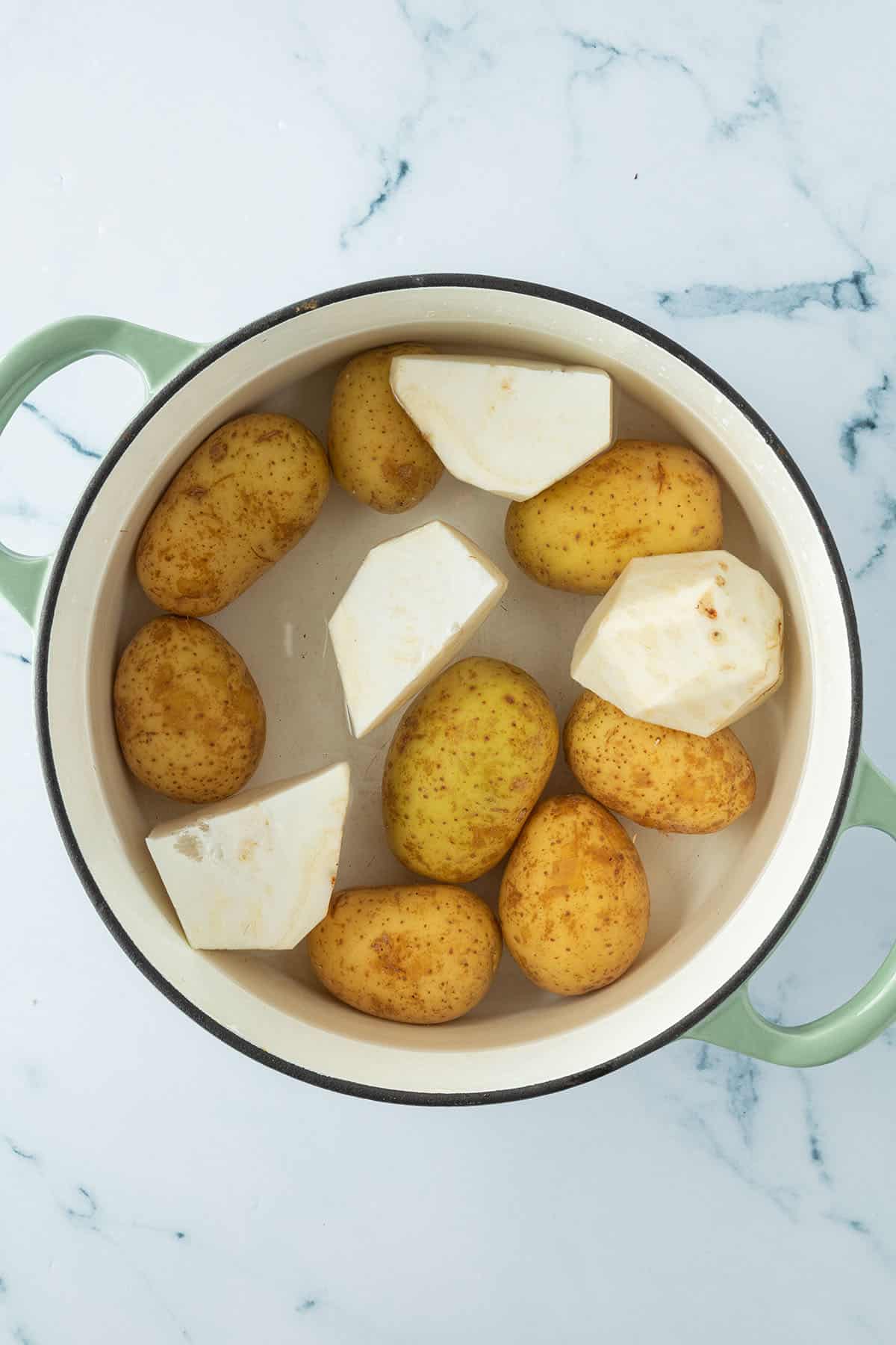 Ungekochte Kartoffeln und Selleriest&uuml;cke in einem Topf mit Wasser.