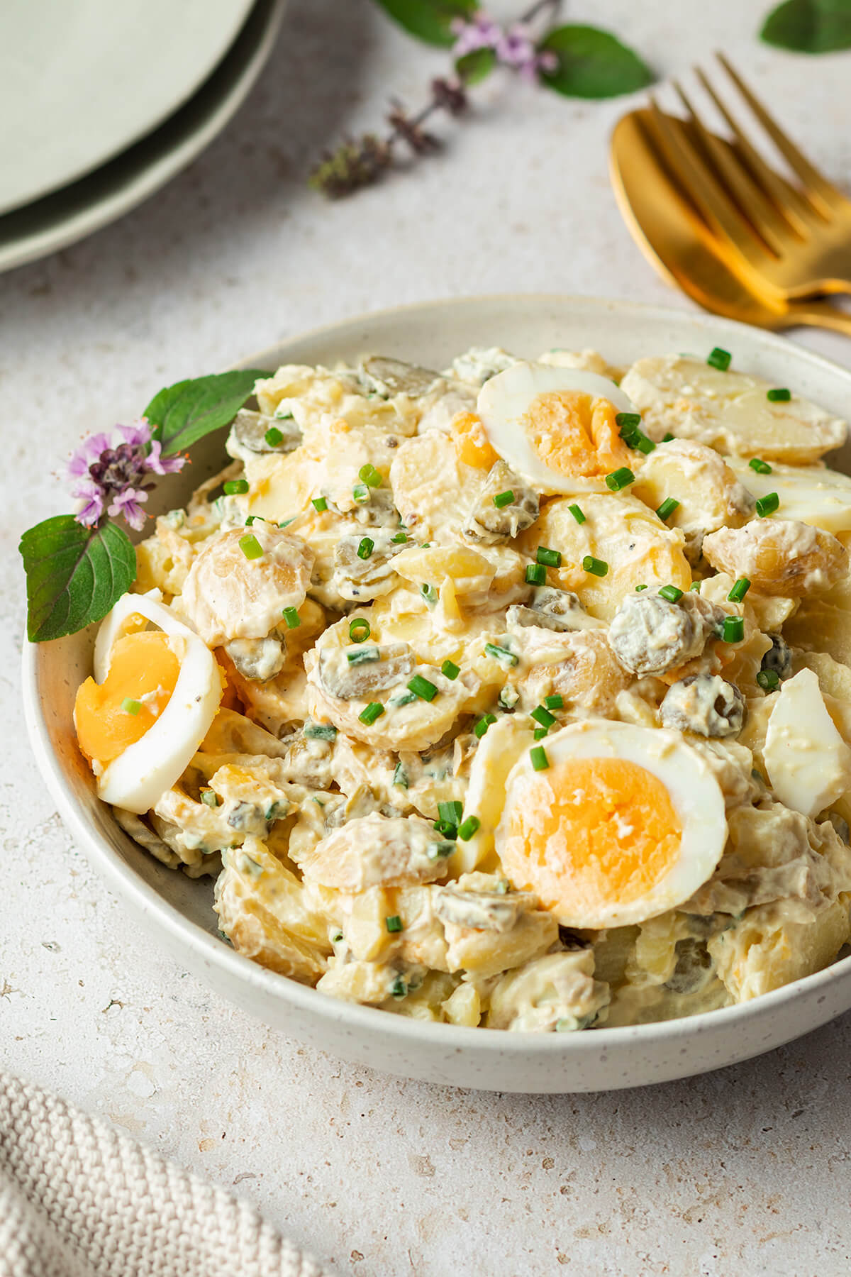 Kartoffelsalat mit Joghurt und Ei serviert in einer gro&szlig;en Sch&uuml;ssel, im Hintergrund liegt Besteck und weitere Teller.