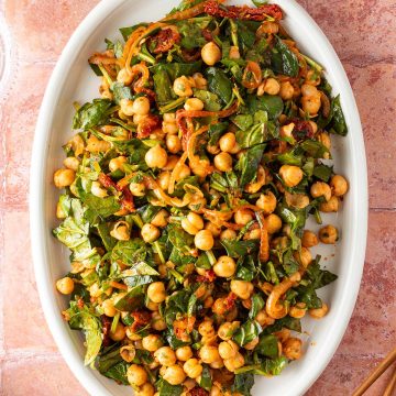 Orientalisch inspirierter Kichererbsensalat mit Spinat und Kr&auml;utern auf einem gro&szlig;en Servierteller.