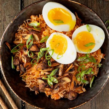 Kimchi Reis Bowl mit knusprigen Pilzen, wachsweich gekochten Eiern und Fr&uuml;hlingszwiebeln auf einem Holzuntergrund.