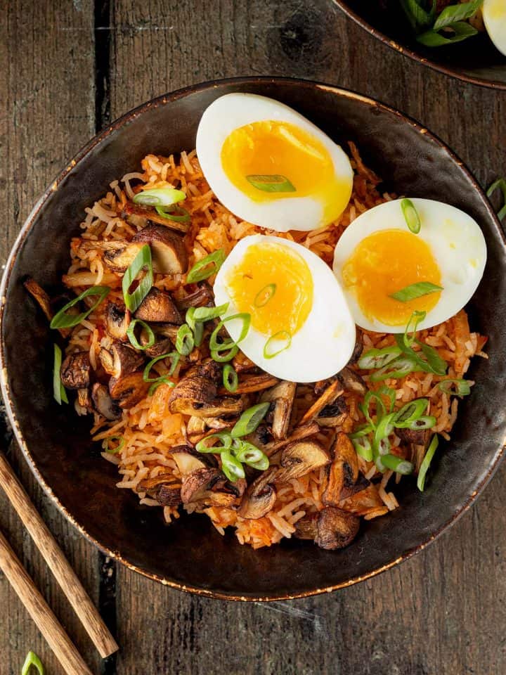 Kimchi Reis Bowl mit knusprigen Pilzen, wachsweich gekochten Eiern und Fr&uuml;hlingszwiebeln auf einem Holzuntergrund.