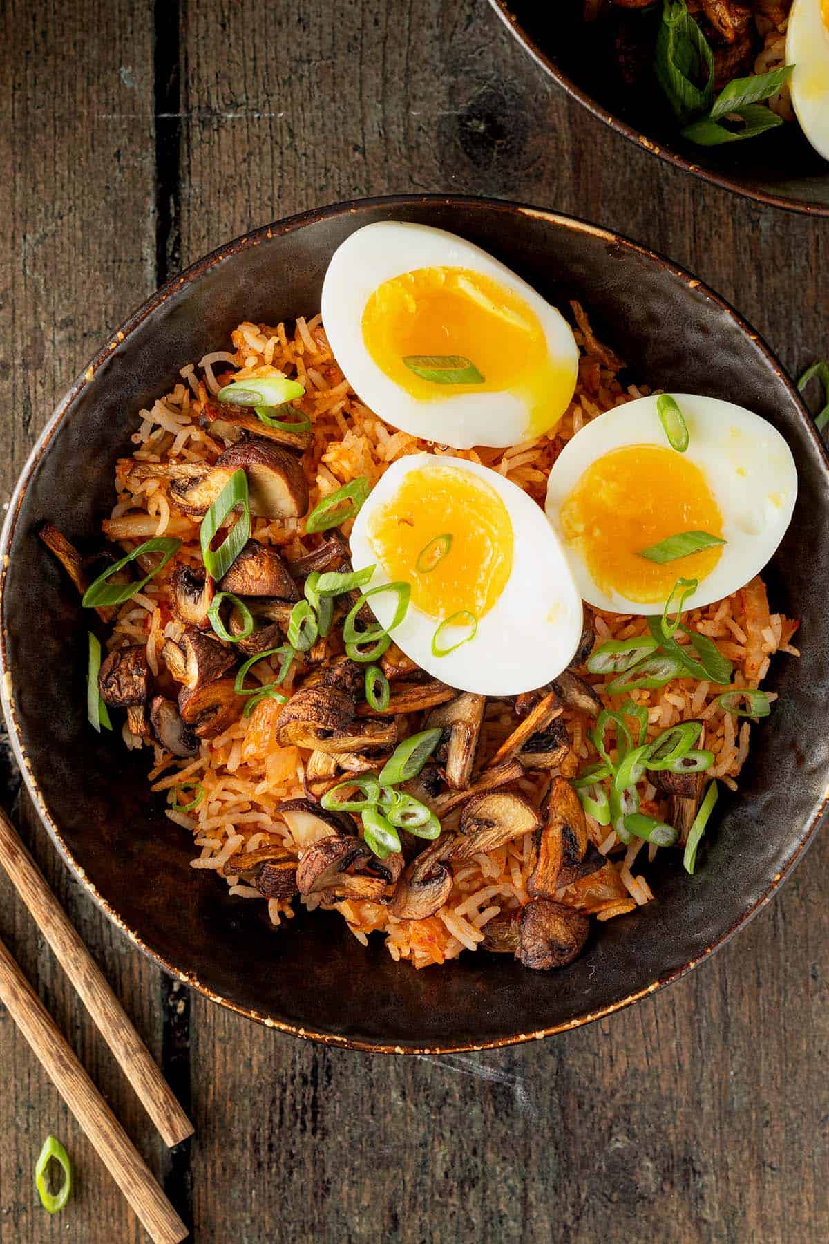 Kimchi Reis Bowl mit knusprigen Pilzen, wachsweich gekochten Eiern und Fr&uuml;hlingszwiebeln auf einem Holzuntergrund.