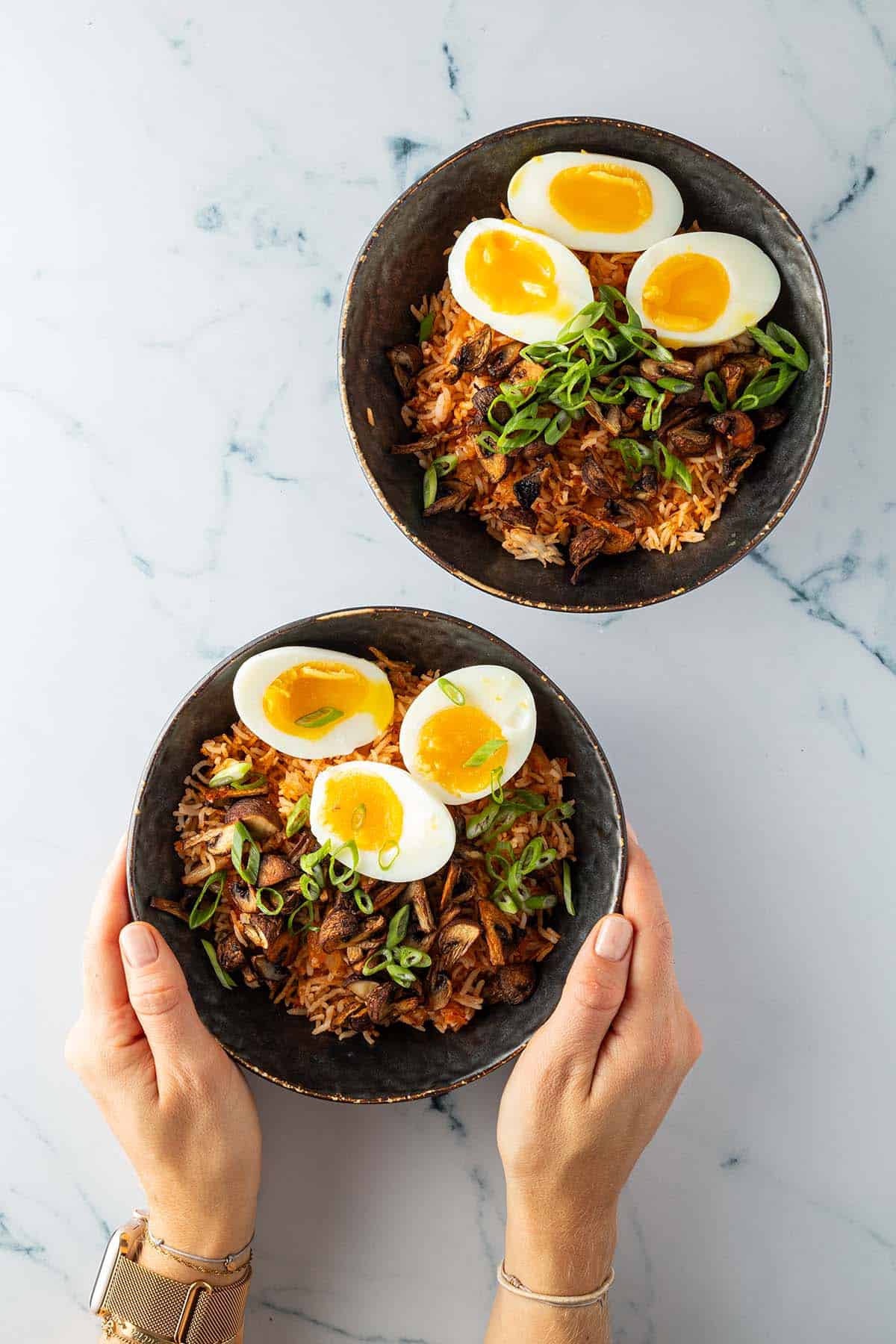 Zwei Bowls mit Kimchi Reis, Eiern und knusprigen Pilzen, garniert mit Fr&uuml;hlingszwiebeln.