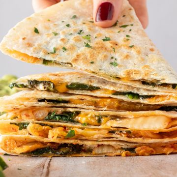 Ein Stapel Quesadillas, von dem einen Hand den ein St&uuml;ck wegnimmt.