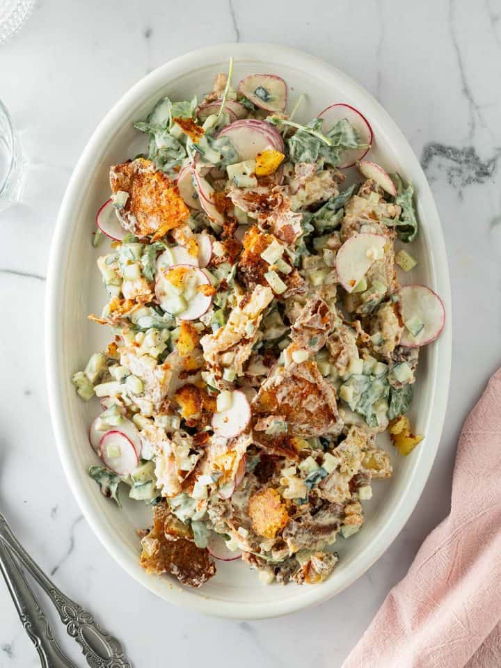 Knuspriger Kartoffelsalat mit ger&ouml;steten Kartoffeln, Gurken, Radieschen und einem cremigen Dressing, Gl&auml;ser un Besteck im Bildrand.