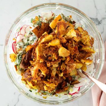 Knusprige Quetschkartoffeln in einer Sch&uuml;ssel mit Gem&uuml;se und einem cremigen Dressing.
