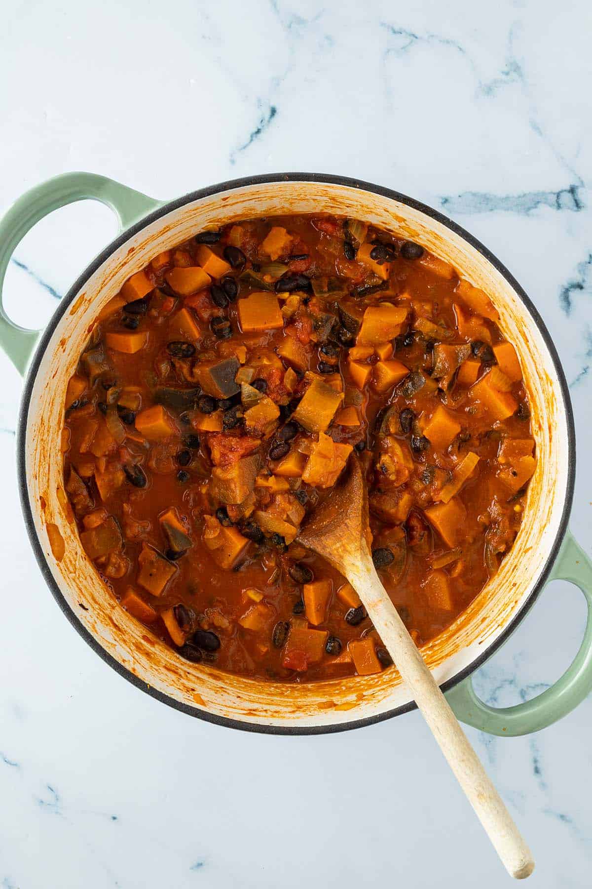 Fertiges Auberginen K&uuml;rbis Curry im Topf mit einem Kochl&ouml;ffel.
