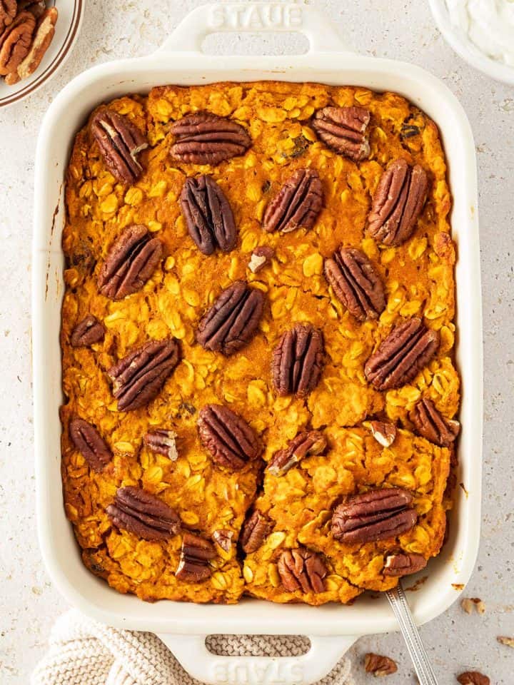 Ein Auflaufform mit einem orangefarbenes Baked Oatmeal mit Pecan N&uuml;ssen auf der Oberfl&auml;che und Deko im Bildrand.