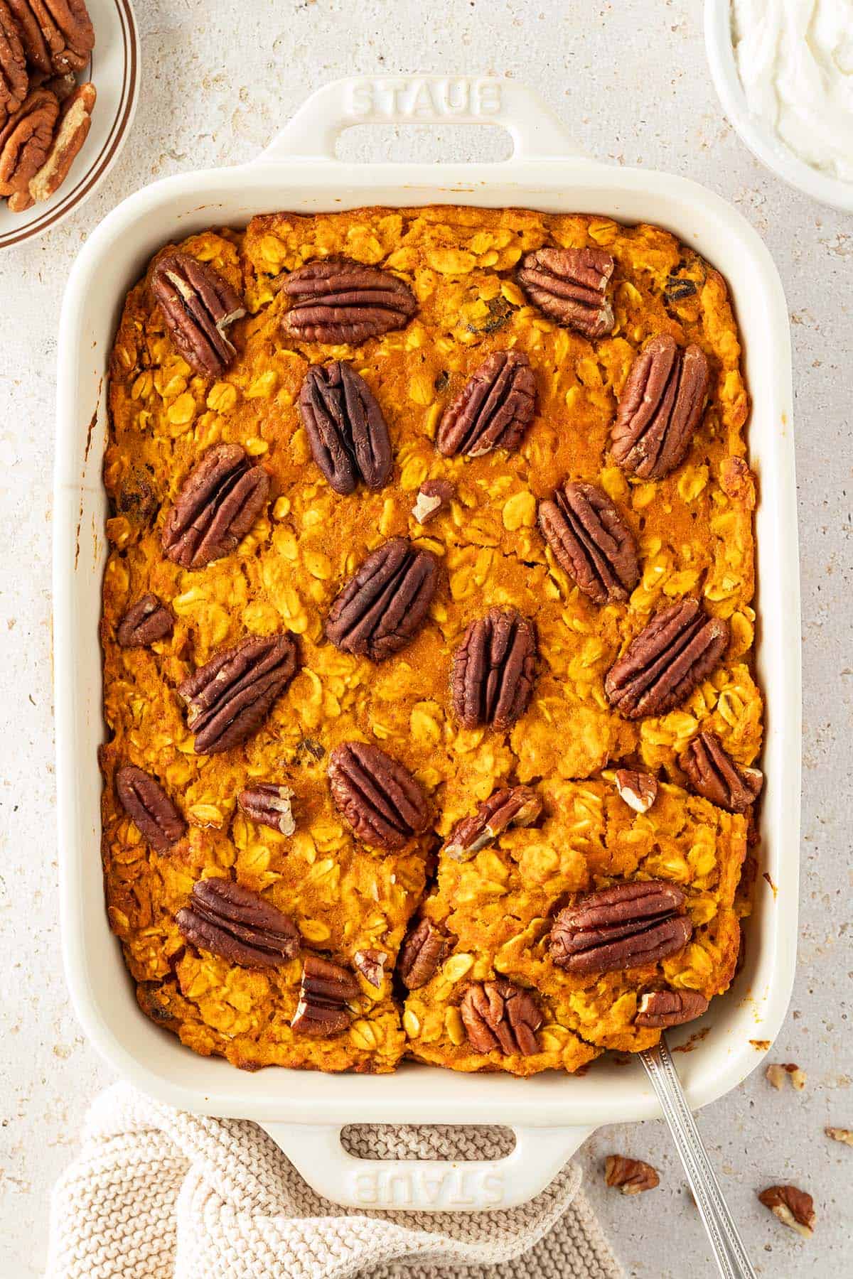 Ein Auflaufform mit einem orangefarbenes Baked Oatmeal mit Pecan N&uuml;ssen auf der Oberfl&auml;che und Deko im Bildrand.