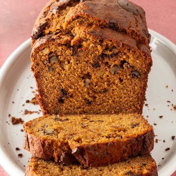 K&uuml;rbis-Bananenbrot aufgeschnitten auf einem ovalen roten Teller auf einem roten Untergrund.