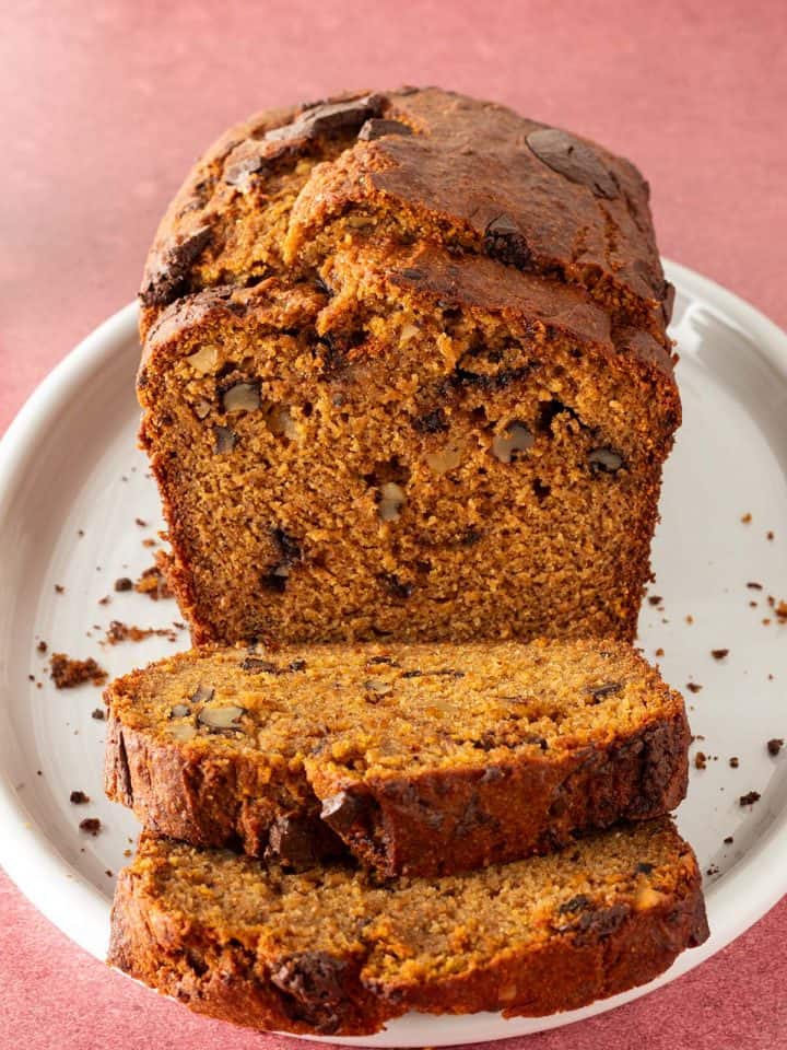 K&uuml;rbis-Bananenbrot aufgeschnitten auf einem ovalen roten Teller auf einem roten Untergrund.