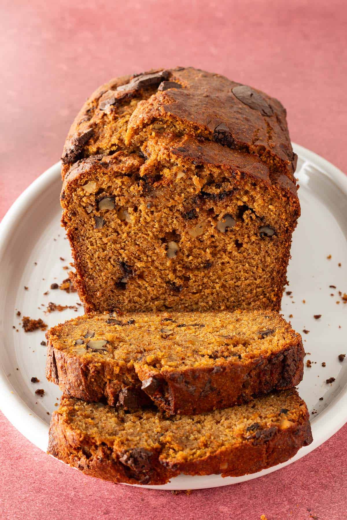 K&uuml;rbis-Bananenbrot aufgeschnitten auf einem ovalen roten Teller auf einem roten Untergrund.