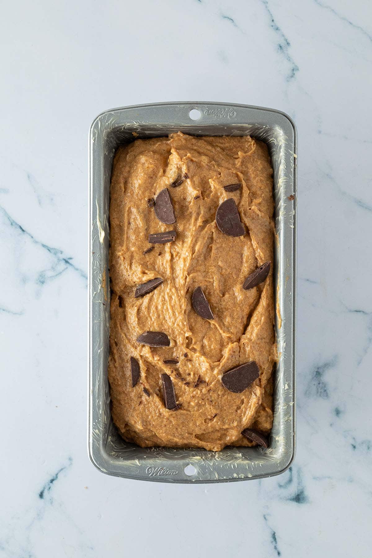 Bananenbrot-Teig in einer mit Butter eingefetteten Kastenform, mit Schokost&uuml;ckchen auf der Oberfl&auml;che.