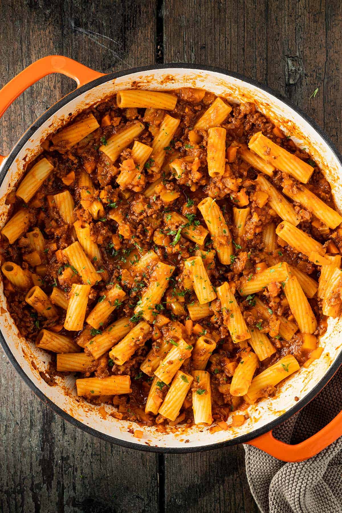 Eine gro&szlig;e Servierpfanne mit Rigatoni Nudeln in einer K&uuml;rbis-Bolognese-Sauce auf einem dunkeln Holzuntergrund.
