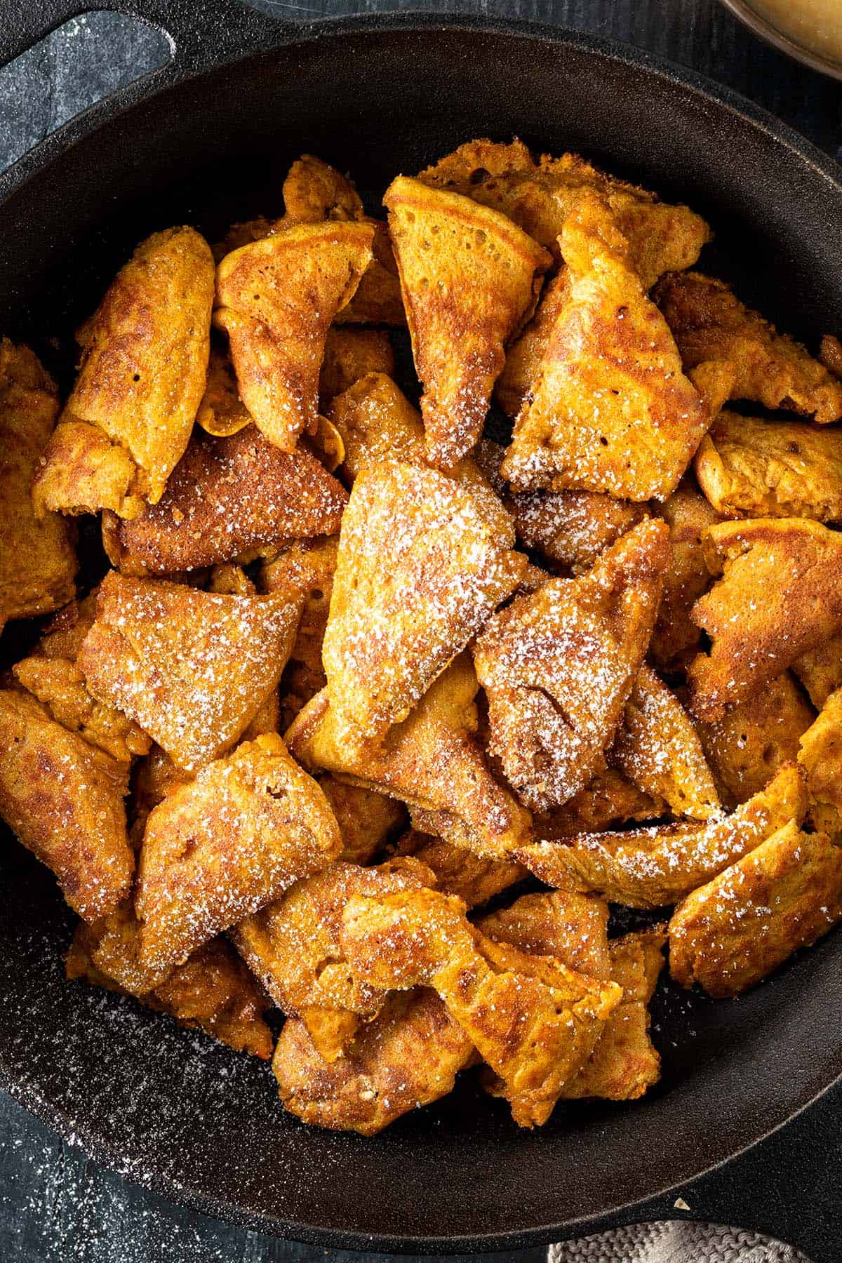 Goldbraune Kaiserschmarrnst&uuml;cke in einer schwarzen Gusseisenpfanne mit etwas Puderzucker.