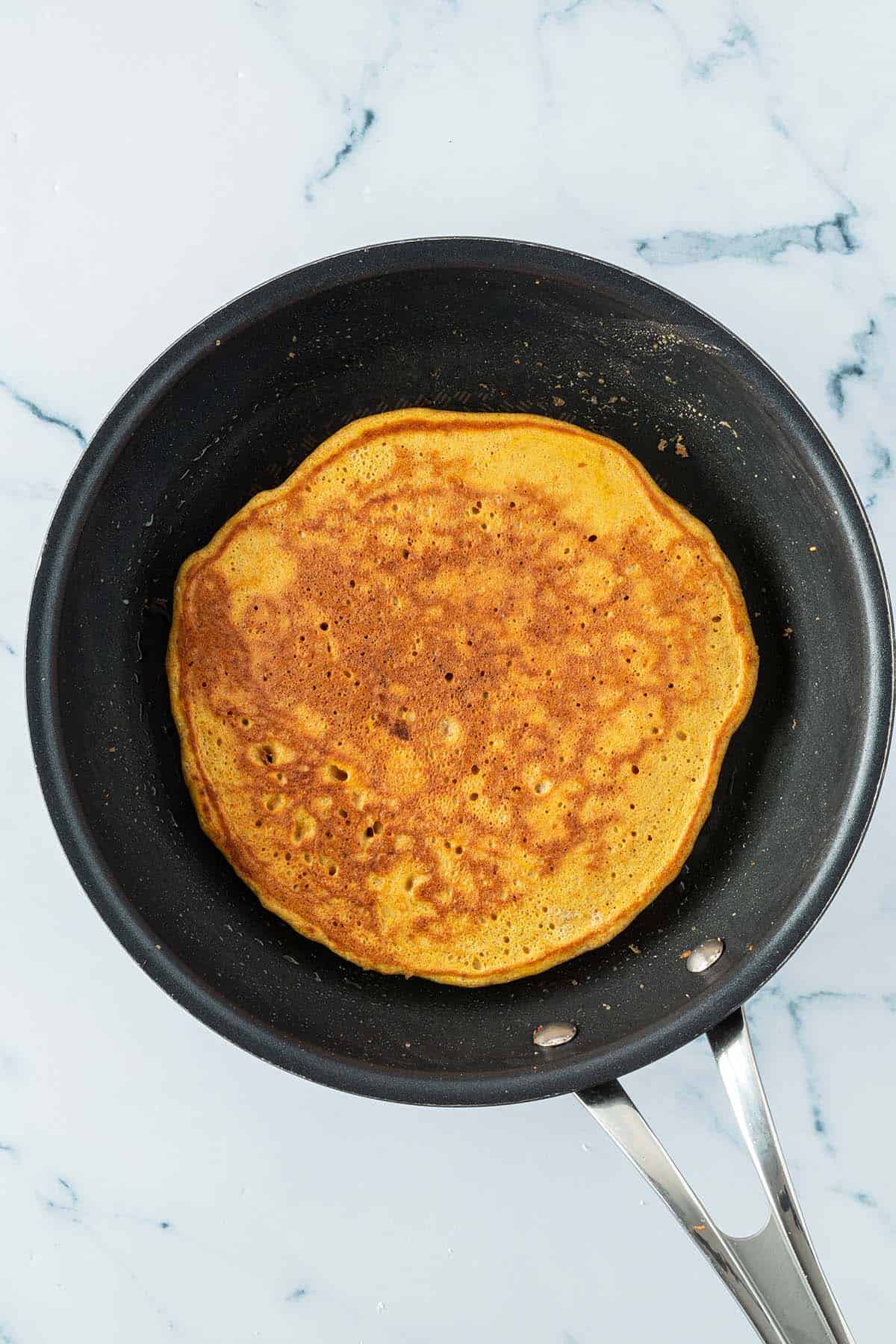 Ein gro&szlig;er dicker Pfannkuchen mit einer goldbraunen Oberseite nach dem Wenden in einer Pfanne.