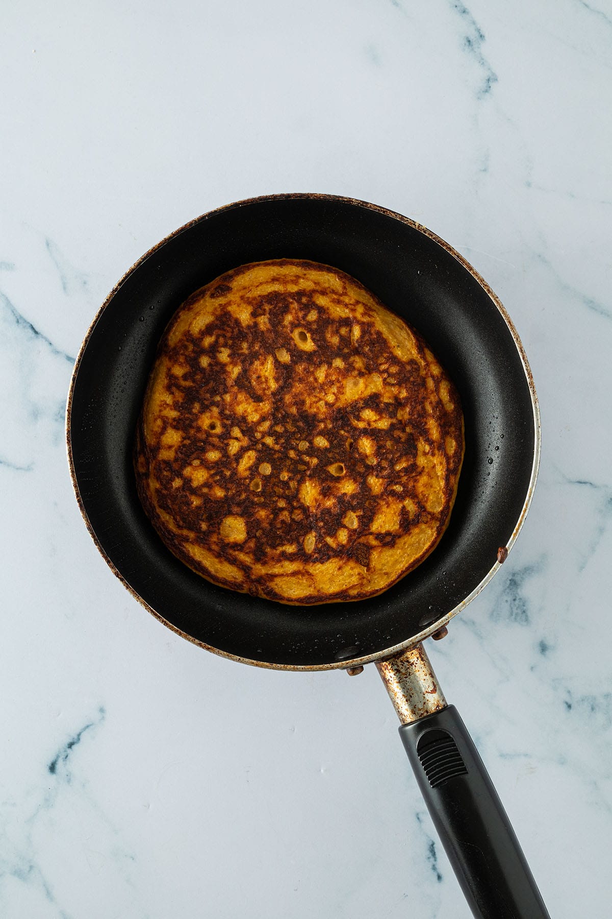 Angebratener, goldbrauner K&uuml;rbis Pancake in einer kleinen Pfanne.