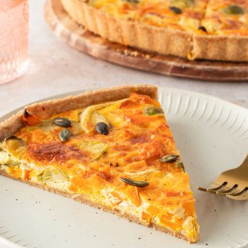 Ein St&uuml;ck K&uuml;rbis Quiche mit Rosenkohl und K&uuml;rbiskernen, die restliche Quiche im Hintergrund.