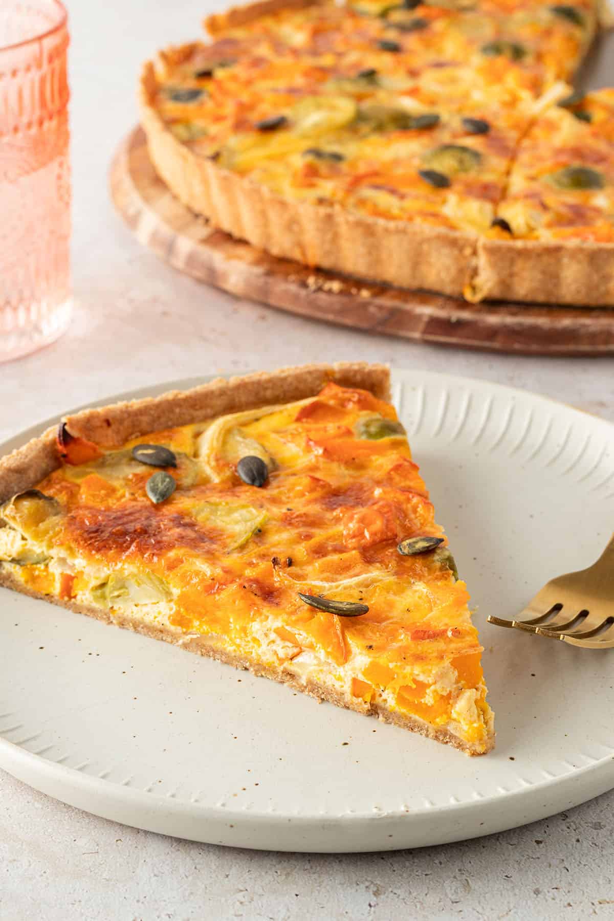 Ein St&uuml;ck K&uuml;rbis Quiche mit Rosenkohl und K&uuml;rbiskernen, die restliche Quiche im Hintergrund.