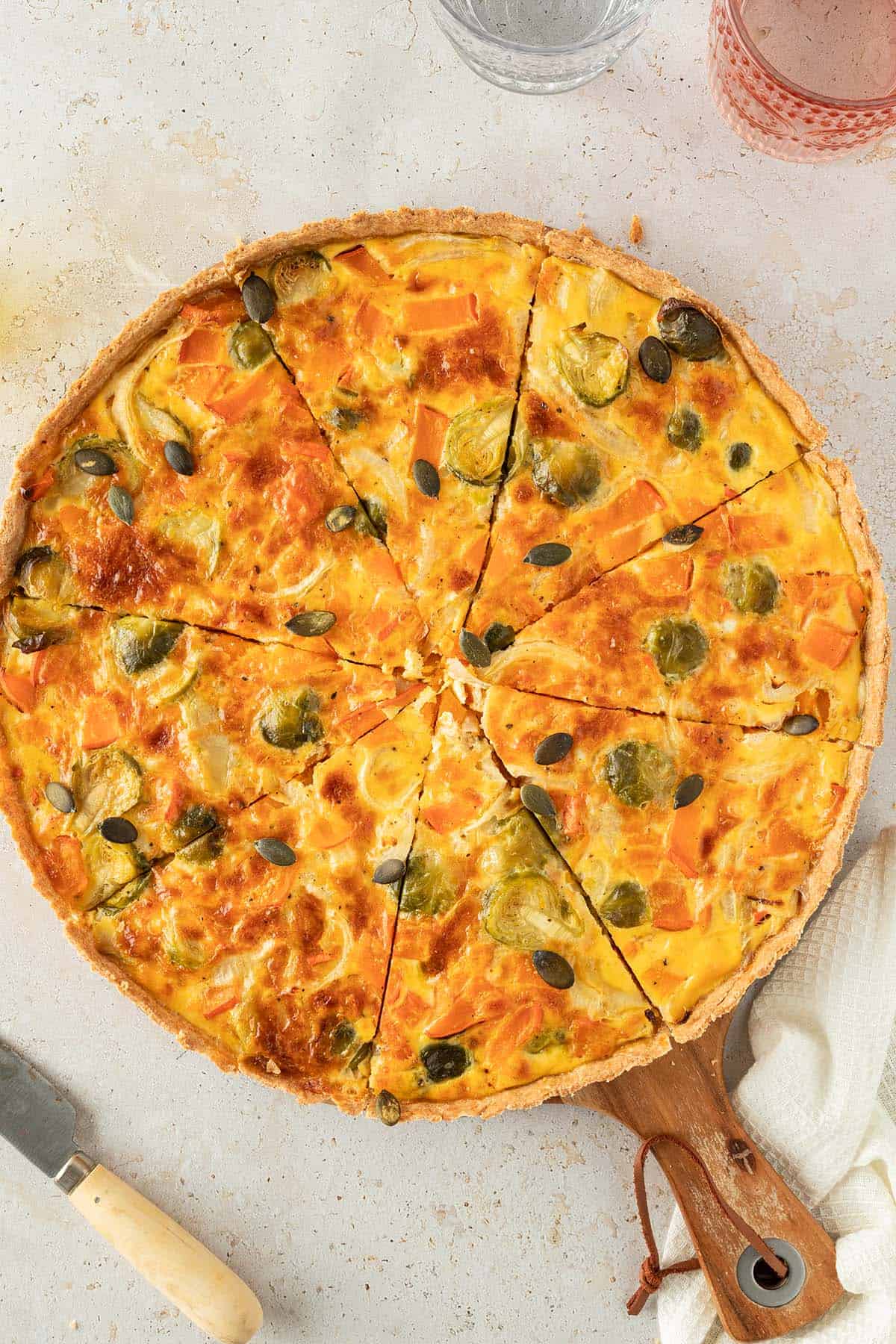 Eine in St&uuml;cke geschnittene Quiche mit K&uuml;rbis und Rosenkohl auf einem hellen Untergrund.