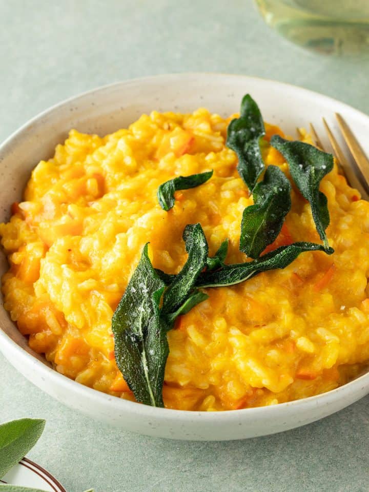Teller mit cremigem K&uuml;rbisrisotto und mit knusprigen Salbei, Deko im Bildrand.